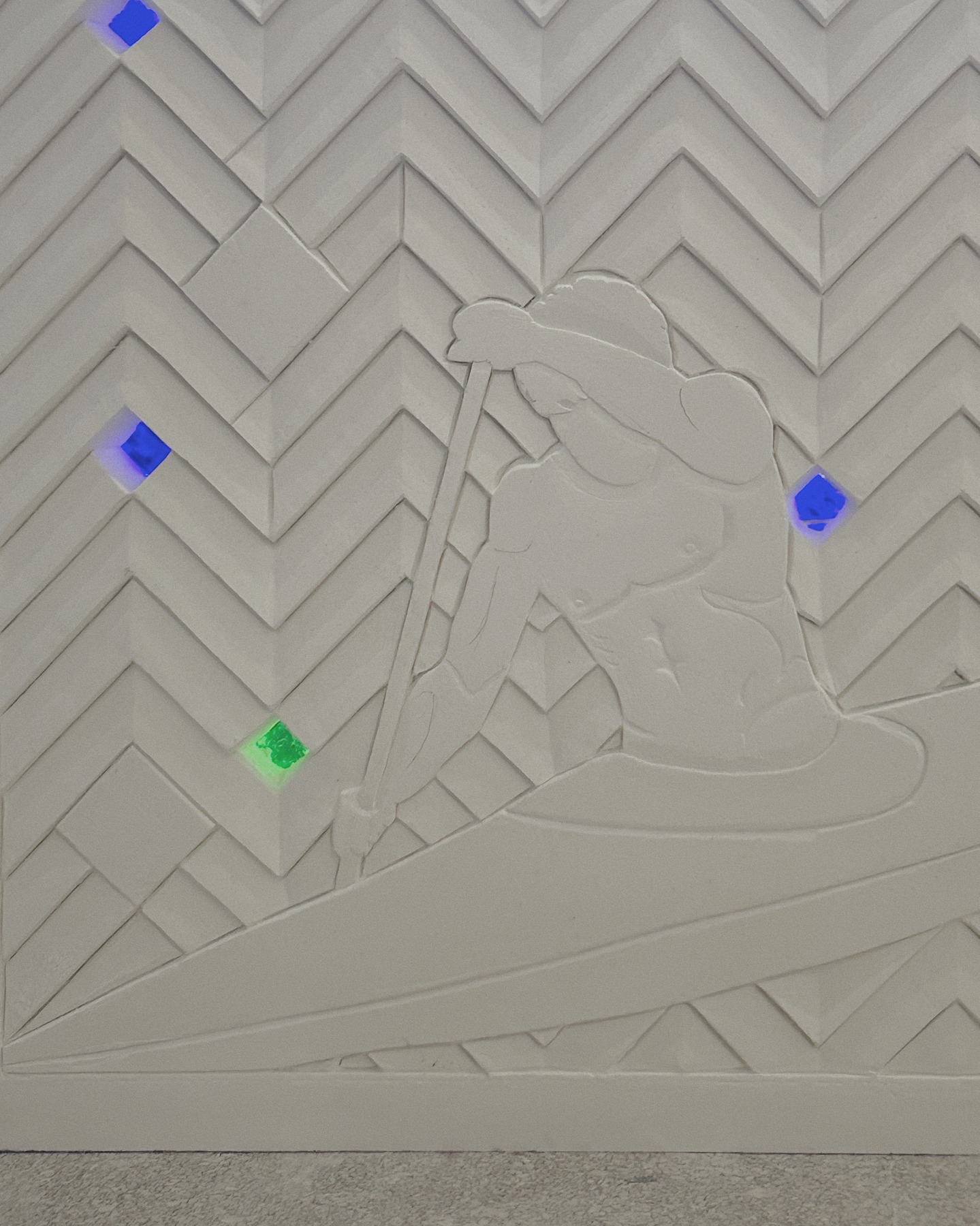 Détail de Kayak Cascade, fresque de plâtre blanc de Louis Barthélemy : un kayakiste pagaie sur un fond de chevrons taillés, incrusté de losanges de verre coloré