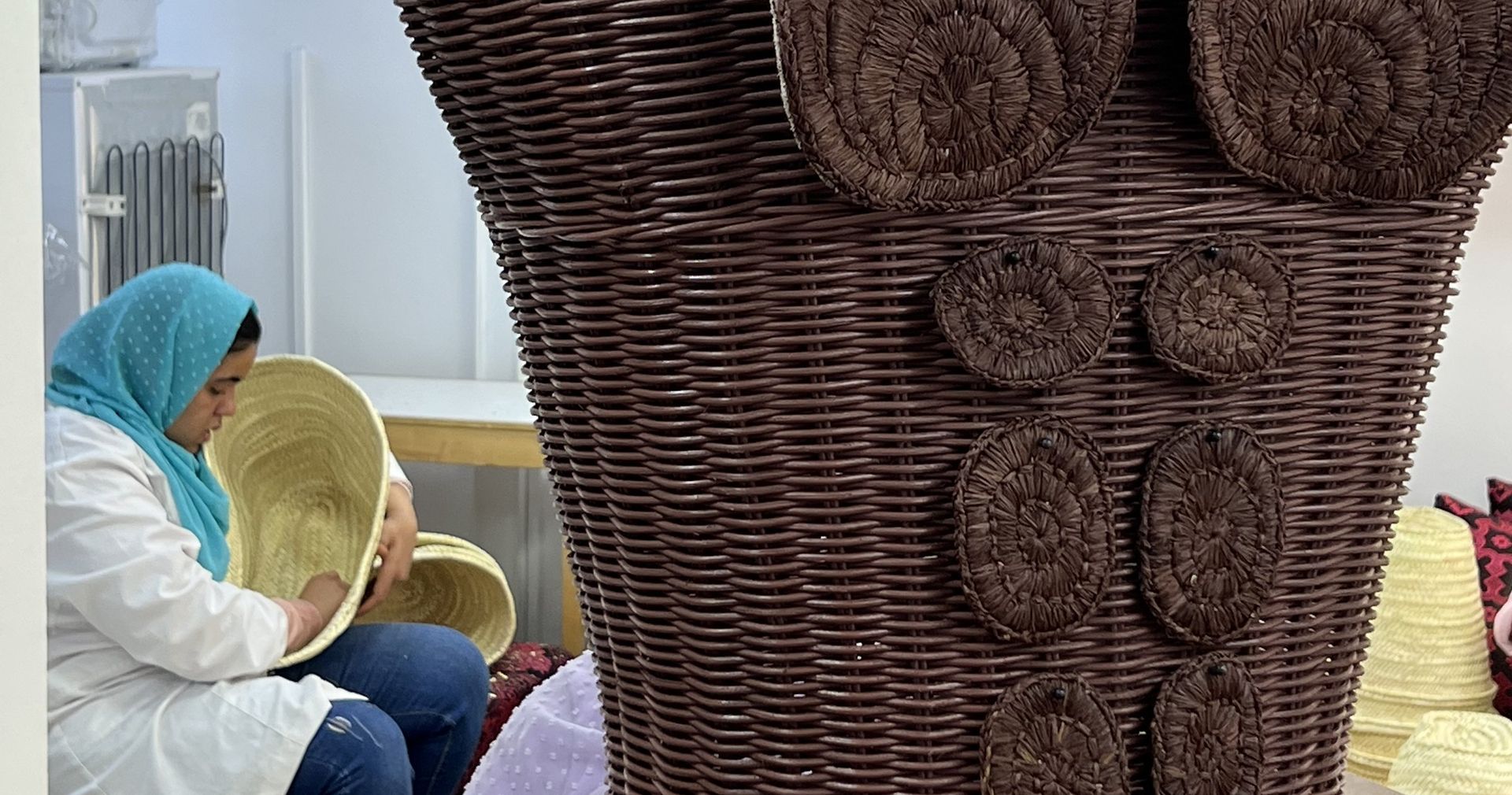 Atelier de vannerie : des artisanes tressent la paille autour d'un buste d'osier posé sur un socle