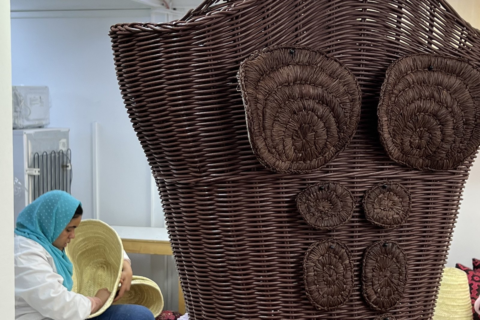 Atelier de vannerie : des artisanes tressent la paille autour d'un buste d'osier posé sur un socle