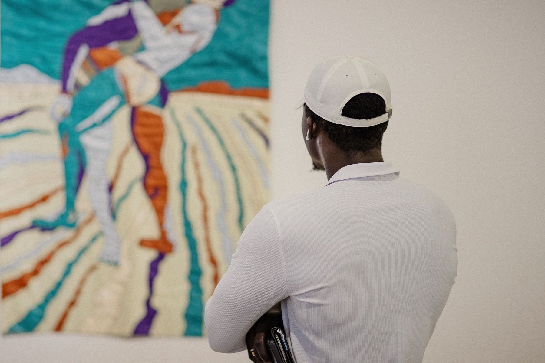 Un visiteur de dos observe une œuvre textile turquoise et orange accrochée sur un mur blanc