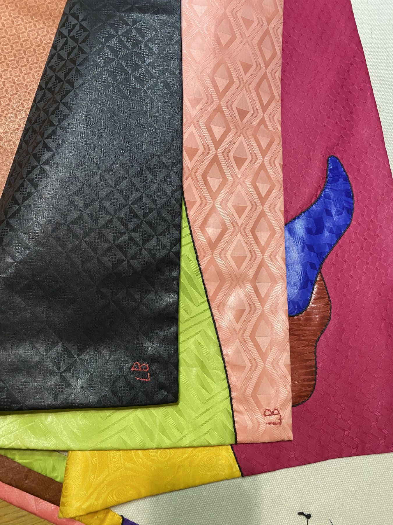 Soies jacquard noire, vert anis, corail et magenta empilées à l'atelier, monogramme LB brodé en rouge