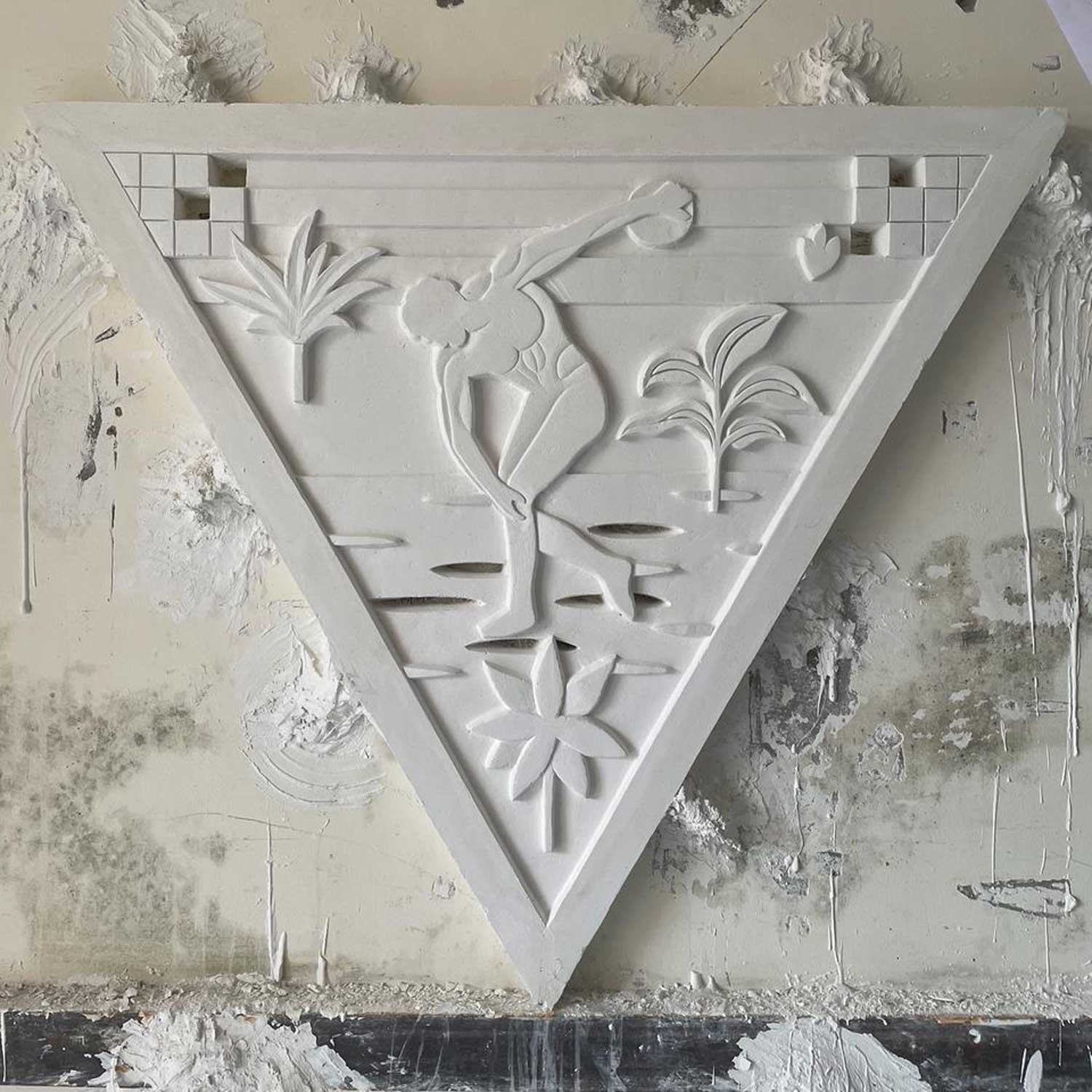 Panneau triangulaire de plâtre à motifs floraux de Louis Barthélemy, accroché au mur maculé d'un atelier