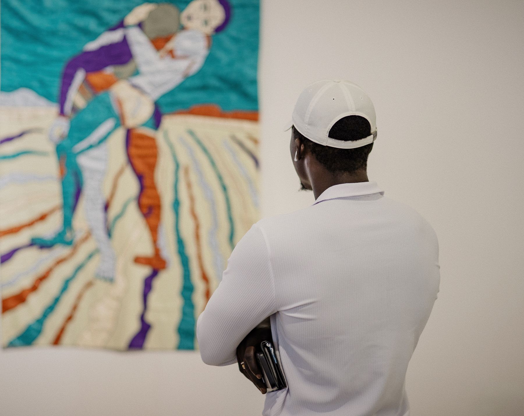 Un visiteur de dos observe une œuvre textile turquoise et orange accrochée sur un mur blanc