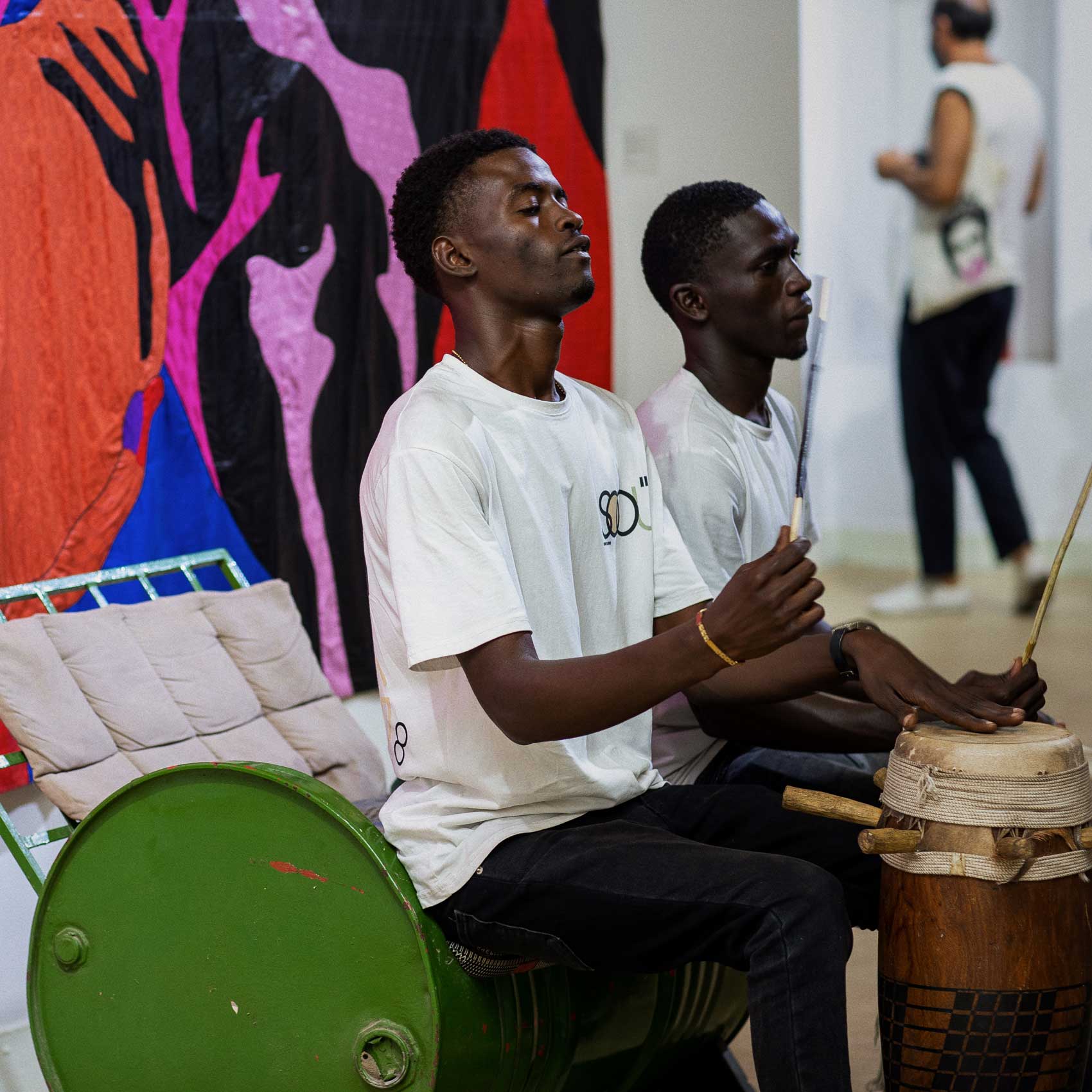 Deux percussionnistes jouent devant une œuvre textile colorée, pendant une soirée à la galerie