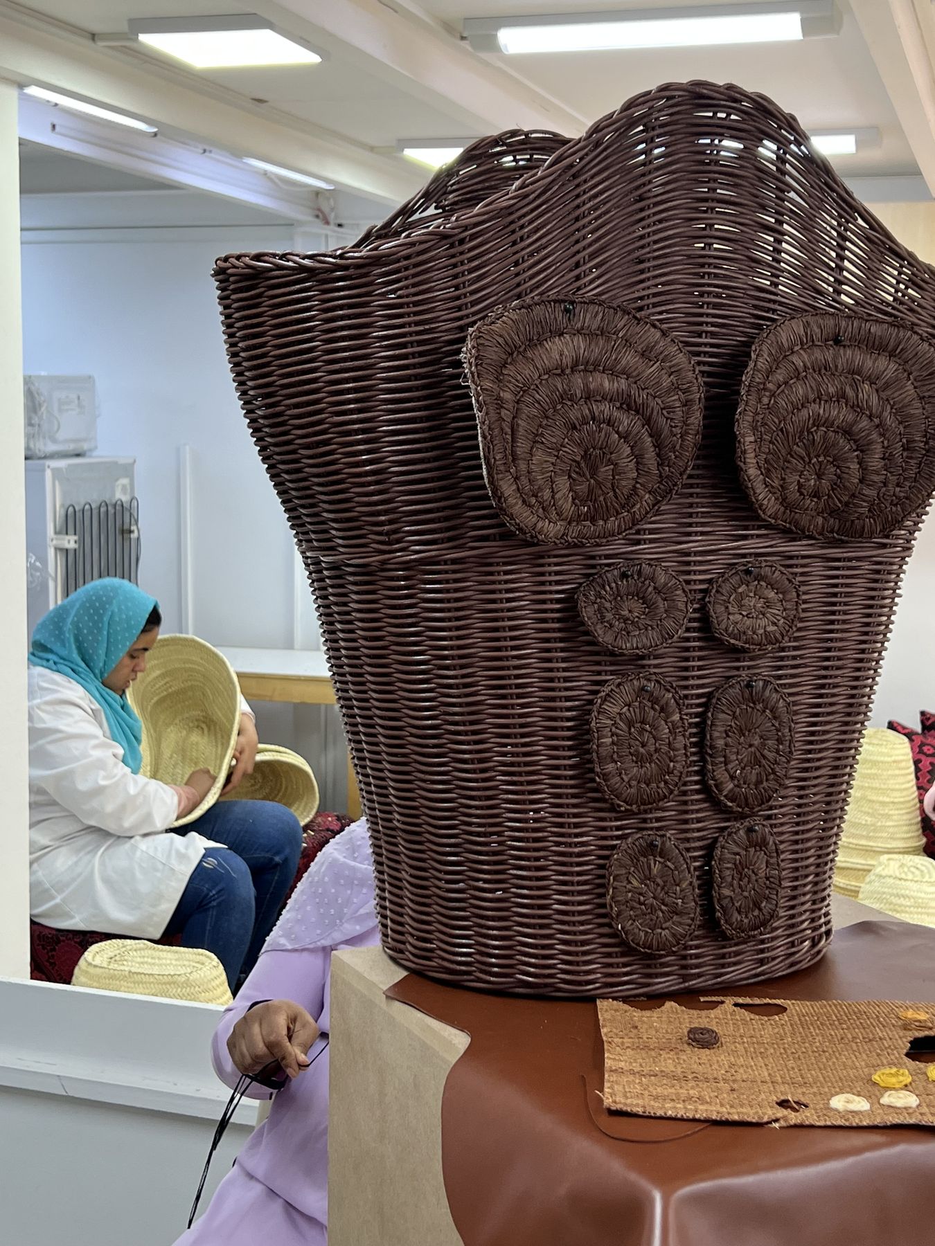 Atelier de vannerie : des artisanes tressent la paille autour d'un buste d'osier posé sur un socle