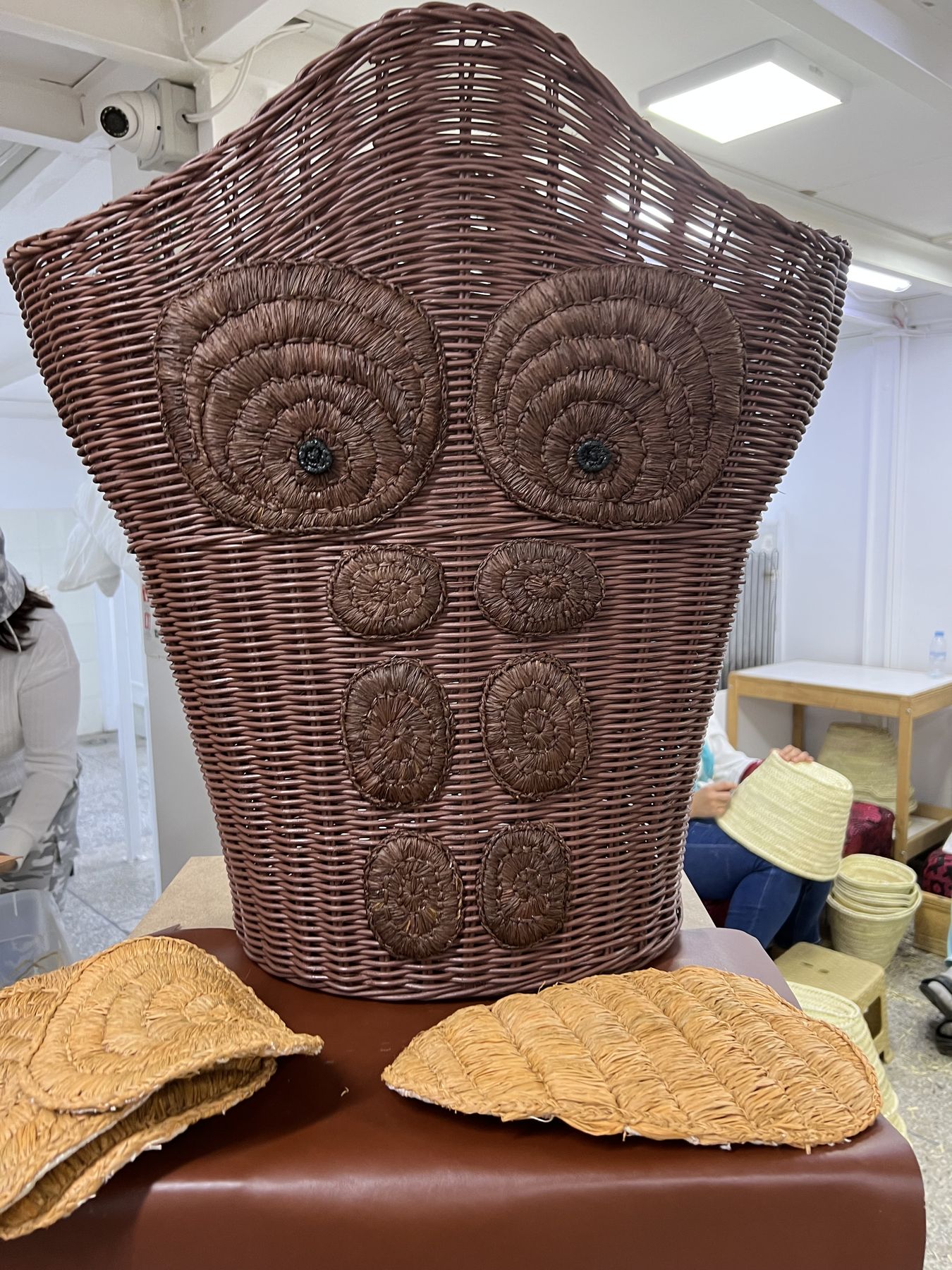 Buste d'osier tressé orné de rosaces, posé sur un socle dans un atelier de vannerie