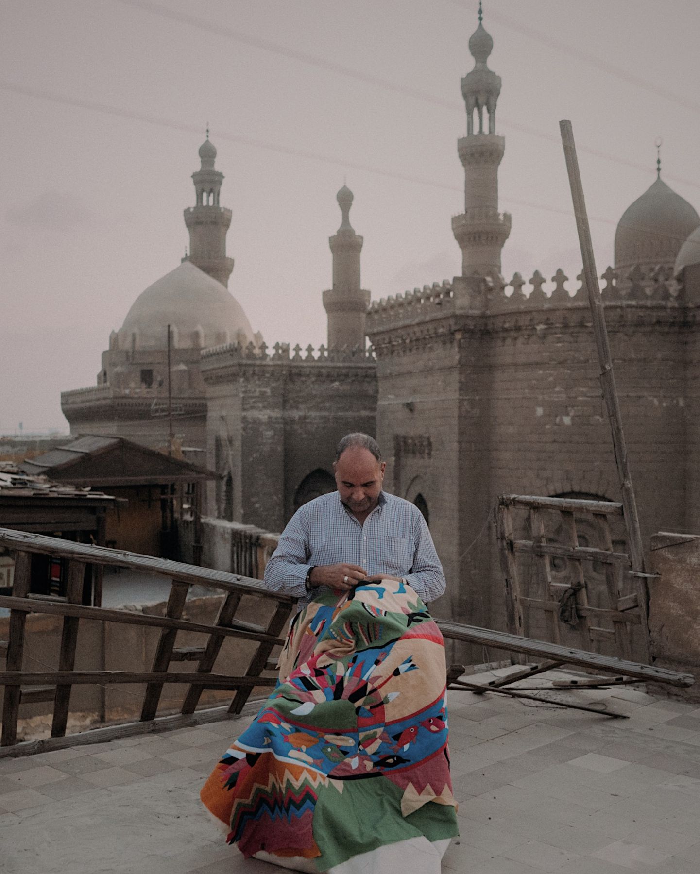 Un artisan coud à la main une grande pièce d'appliqué colorée sur un toit du Caire, coupoles et minarets en arrière-plan