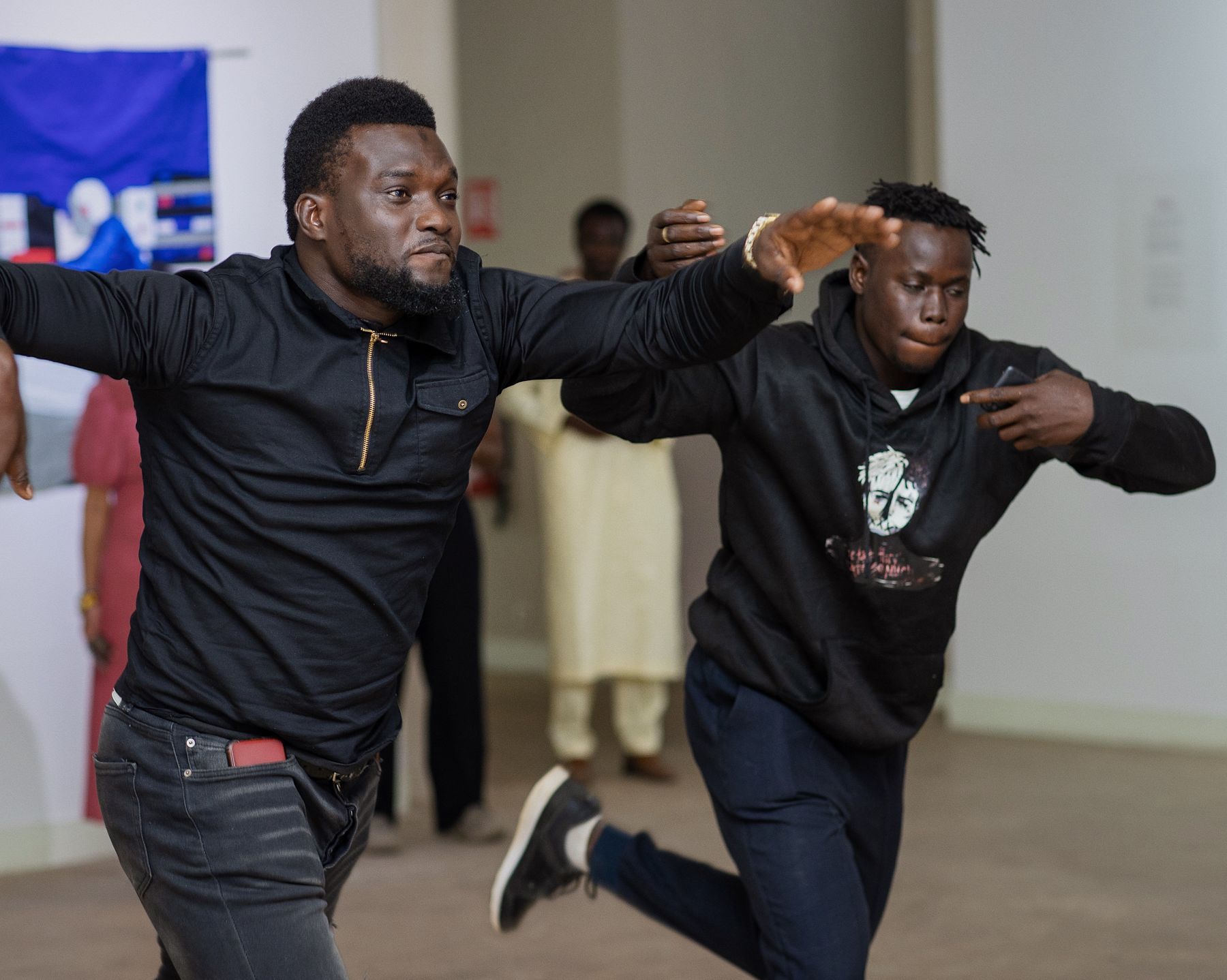 Deux danseurs en mouvement dans la salle d'exposition, devant les œuvres textiles accrochées