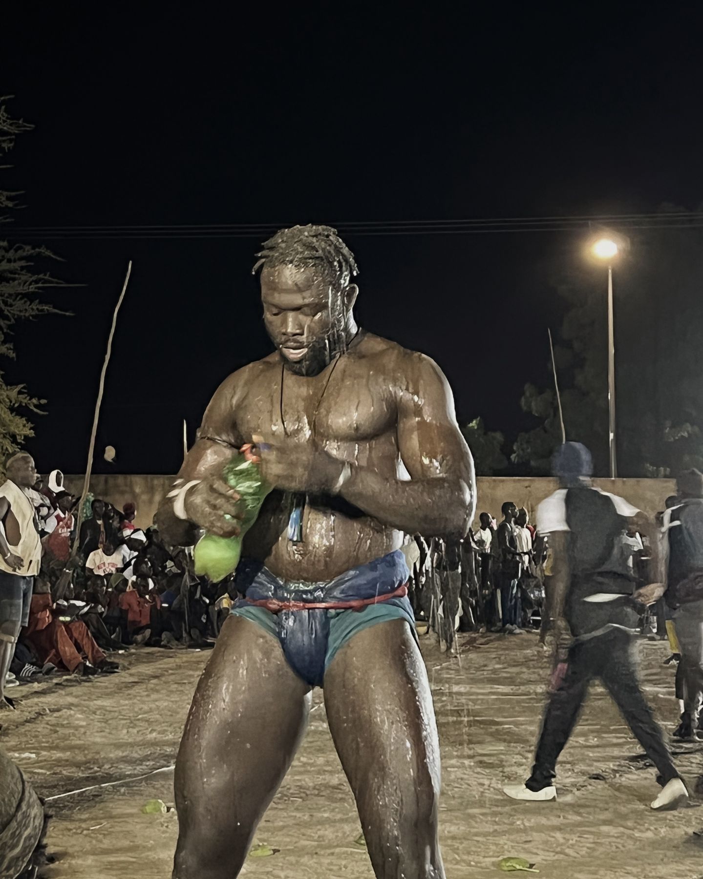 Lutteur sénégalais huilé et couvert de sable, de nuit, devant le public d'une arène